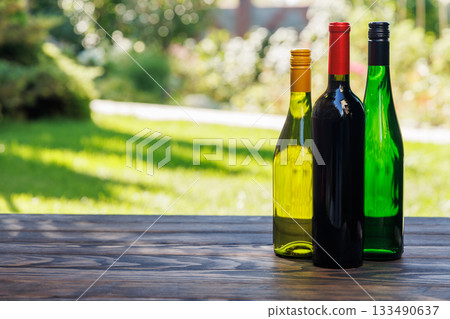 Wine bottles with grapes on a wooden table, glowing with sunny bokeh in the background Wine bottles with grapes on a wooden table, glowing with sunny bokeh in the background 133490637
