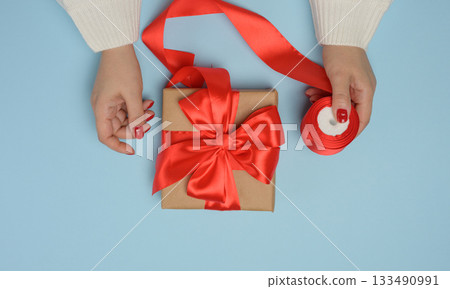 Two female hands holding gift boxes tied with a red ribbon on a blue background 133490991