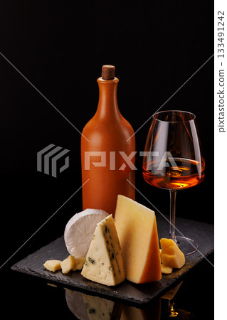 A refined selection of aged cheeses presented on a board, accompanied by a glasses of wine A refined selection of aged cheeses presented on a board, accompanied by a glasses of wine 133491242