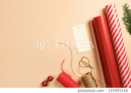 Christmas gift wrapping with red and white striped wrapping paper, rope, baubles, scissors, thuja spruce on beige backdrop. Copy space. Christmas gift wrapping with red and white striped wrapping paper, rope, baubles, scissors, thuja spruce on beige backdrop. Copy space. 133491316