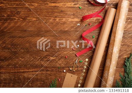 Christmas wrapping background with paper rolls, ribbon, and scissors on dark wooden desk. Copy space for text. Christmas wrapping background with paper rolls, ribbon, and scissors on dark wooden desk. Copy space for text. 133491318