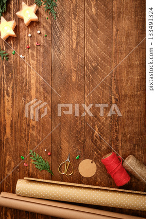Christmas wrapping background with paper rolls, rope, gift tags and scissors on dark wooden desk. Copy space for text. Christmas wrapping background with paper rolls, rope, gift tags and scissors on dark wooden desk. Copy space for text. 133491324