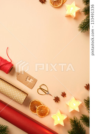 Christmas gift wrapping with star candles, dried oranges, spices, and wrapping paper on beige background. Place for text or design. Christmas gift wrapping with star candles, dried oranges, spices, and wrapping paper on beige background. Place for text or design. 133491336