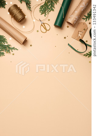 Gift wrapping background. Paper rolls, twine, gift tag, and gold stars on beige table. Copy space for holiday text or design. Gift wrapping background. Paper rolls, twine, gift tag, and gold stars on beige table. Copy space for holiday text or design. 133491342