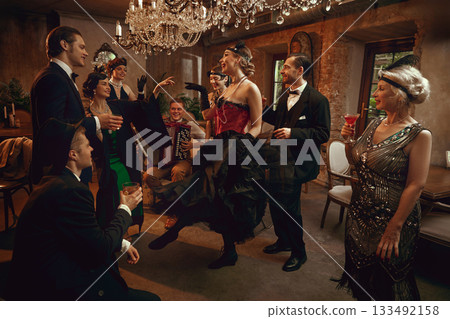 Retro friends gathered around dancer performing in vintage bar under crystal chandelier Retro friends gathered around dancer performing in vintage bar under crystal chandelier 133492158
