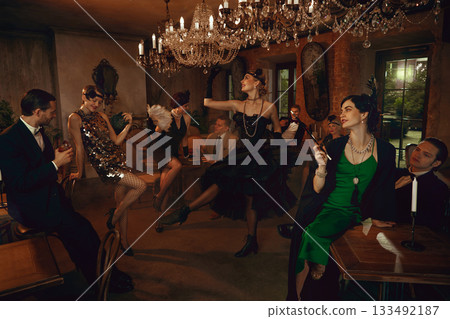 Group of retro friends celebrating and dancing under chandelier in glamorous vintage bar Group of retro friends celebrating and dancing under chandelier in glamorous vintage bar 133492187