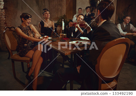 Vintage dinner party with stylish friends toasting and enjoying festive retro evening 133492190