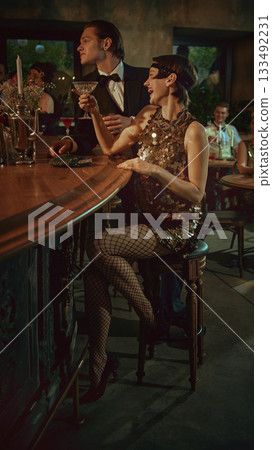 Laughing young woman in sparkling retro dress enjoying cocktails at vintage bar 133492231