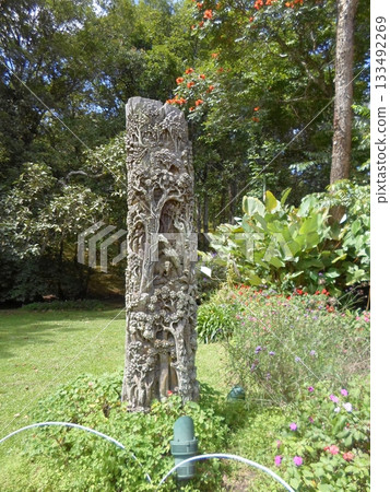 A Detailed Carved Wooden Sculpture Standing Tall in a Lush Garden with Red Flowers 133492269