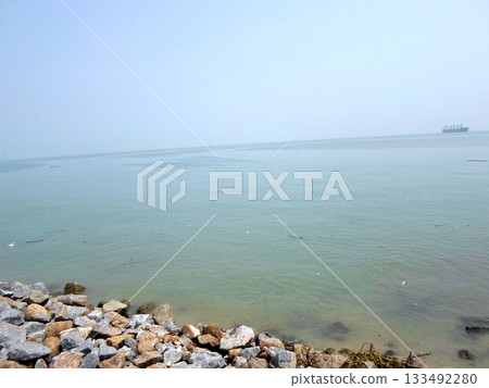 A Serene Coastal View with Calm Waters, Rocky Shoreline, and a Distant Ship on the Horizon A Serene Coastal View with Calm Waters, Rocky Shoreline, and a Distant Ship on the Horizon 133492280