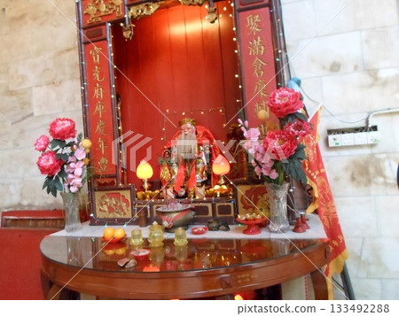 A Temple Altar Adorned with a Statue, Pink Flowers, and Red Decorative Elements A Temple Altar Adorned with a Statue, Pink Flowers, and Red Decorative Elements 133492288