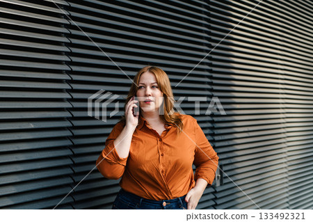 Curvy adult woman making phone call outdoors. 133492321