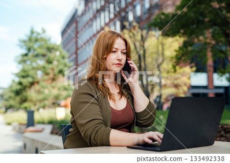 Curvy woman working outdoors, typing on laptop and making call. Curvy woman working outdoors, typing on laptop and making call. 133492338