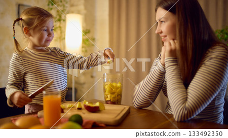 Fresh orange juice on table during fun fruit prep with mother and daughter cheerful mood 133492350