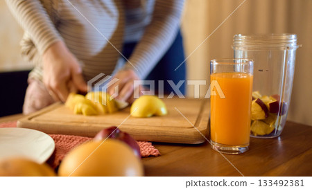 Orange juice glass on table during fruit cutting with warm mother and daughter mood Orange juice glass on table during fruit cutting with warm mother and daughter mood 133492381