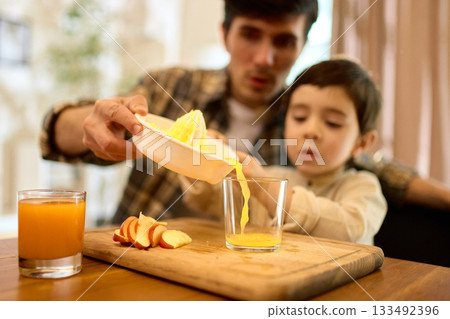 Fresh squeezed citrus juice poured by father and son into glass with warm kitchen mood 133492396