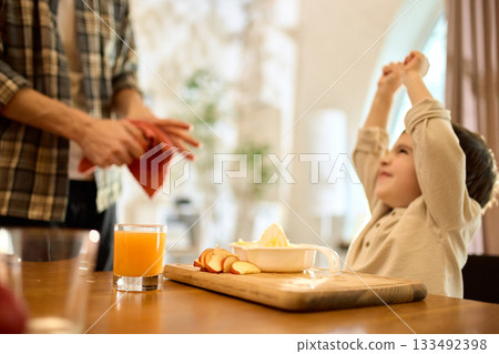 Orange juice in glass with happy son celebrating fresh citrus squeezing in warm kitchen 133492398