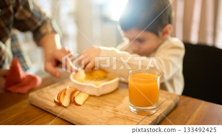 Orange juice in glass beside father guiding son squeezing fruit with warm emotional mood Orange juice in glass beside father guiding son squeezing fruit with warm emotional mood 133492425