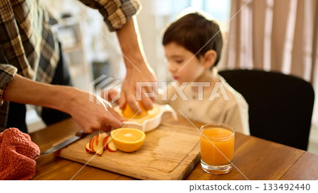 Fresh orange juice on table with father and son squeezing citrus in sunny kitchen atmosphere 133492440