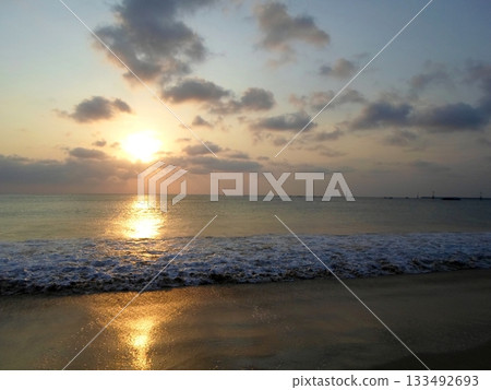 Serene Sunset on a Beach with a Cloudy Sky and Waves Lapping at the Shoreline 133492693