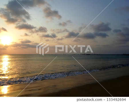 Tranquil Sunset on a Beach with Distant Structures Silhouetted Against the Horizon Tranquil Sunset on a Beach with Distant Structures Silhouetted Against the Horizon 133492694