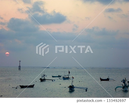 Warm Sunset Over the Ocean with Traditional Boats Floating Near the Horizon 133492697