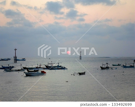 Calm Sunset Over the Ocean with Boats and a Platform Silhouetted Against the Sky Calm Sunset Over the Ocean with Boats and a Platform Silhouetted Against the Sky 133492699