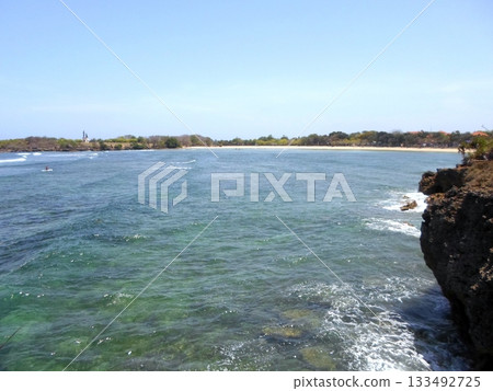 Rocky Cliff Overlooking a Sandy Beach with Surfers Riding Waves on a Clear Day Rocky Cliff Overlooking a Sandy Beach with Surfers Riding Waves on a Clear Day 133492725