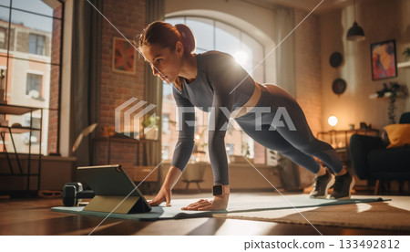 Young Woman Doing Plank Exercise at Home with Online Workout 133492812