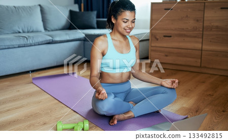 Young Woman Meditating at Home During Online Yoga Session Young Woman Meditating at Home During Online Yoga Session 133492815