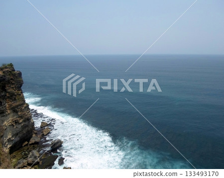 A Cliffside View of the Ocean with Waves Crashing Against Rocks Under a Clear Blue Sky 133493170