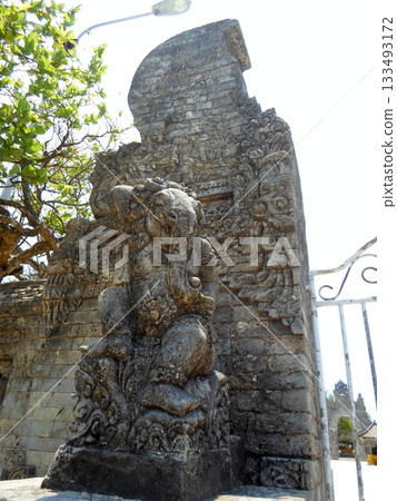 A Stone Ganesha Statue at a Temple Entrance with Intricate Carvings and Greenery in the Background A Stone Ganesha Statue at a Temple Entrance with Intricate Carvings and Greenery in the Background 133493172
