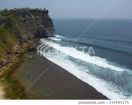 A Cliffside Ocean Scape with Waves Crashing Against a Rocky Shoreline and Greenery on the Cliff 133493175