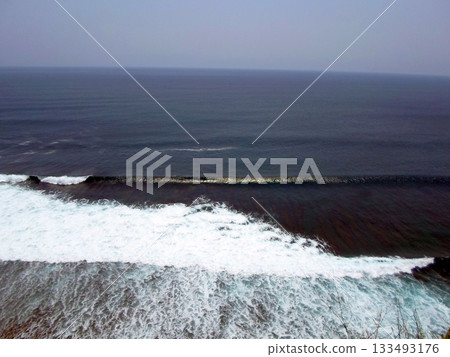 Ocean Waves Crashing Against a Cliffside with a Vast View of the Sea Under a Clear Sky 133493176