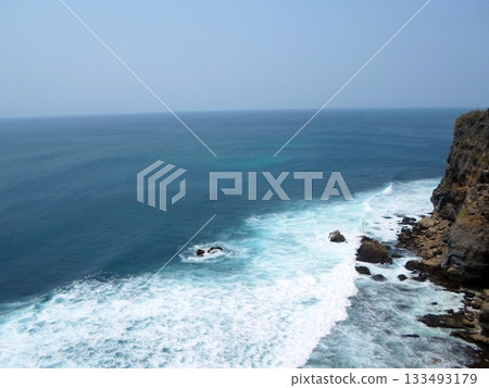 A Panoramic View of Ocean Waves Crashing Against a Cliffside with Rocky Shores Under a Clear Sky A Panoramic View of Ocean Waves Crashing Against a Cliffside with Rocky Shores Under a Clear Sky 133493179