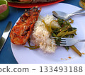 A Plate of Grilled Lobster with Rice and Sauteed Vegetables on a Beachside Table with Utensils 133493188