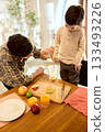Glass of orange juice with father and son adding fruits to blender in sunny kitchen 133493226
