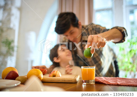 Orange juice glass with soft natural light and cheerful family kitchen atmosphere Orange juice glass with soft natural light and cheerful family kitchen atmosphere 133493233