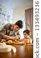 Orange juice glass in bright kitchen scene with lively warm family moment 133493236