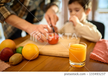 Fresh orange juice in glass with sunny kitchen mood and gentle father and son presence Fresh orange juice in glass with sunny kitchen mood and gentle father and son presence 133493237
