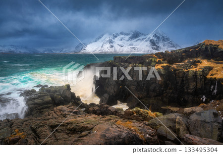 Waves, rocky coastline with turquoise sea and snowy mountains 133495304