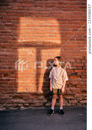 Young girl standing by red brick wall with sunlight 133496037