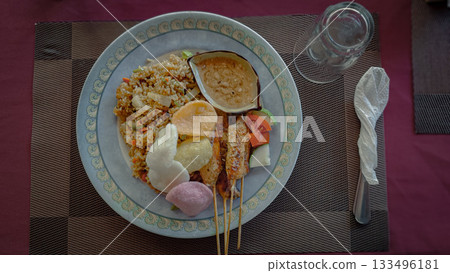 A plate of authentic traditional local Indonesian food featuring fried rice or nasi goreng, sate or satay skewers, and peanut sauce 133496181