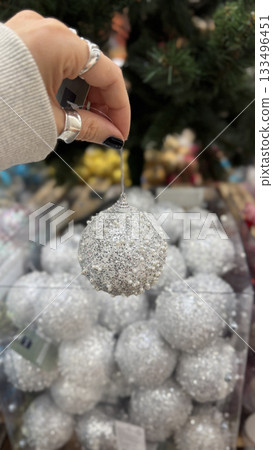 Christmas silver ornament held by hand with black nail polish near festive holiday tree 133496451