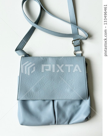 Light blue leather crossbody bag on white table, with adjustable strap and embossed logo Light blue leather crossbody bag on white table, with adjustable strap and embossed logo 133496461