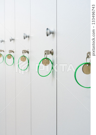 Row of white lockers with green keychains hanging from each lock in a modern facility Row of white lockers with green keychains hanging from each lock in a modern facility 133496743