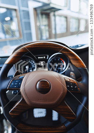 Luxury car interior with wooden steering wheel and dashboard in urban setting 133496769