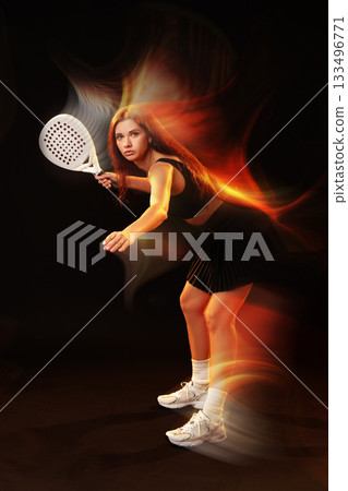 Young athlete prepares for a powerful tennis shot in a dynamic, energetic pose at night 133496771