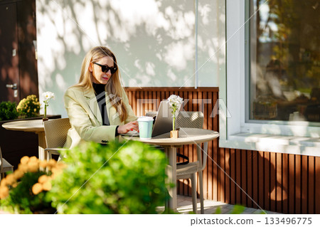 Woman working on laptop at outdoor cafe during sunny day in spring 133496775