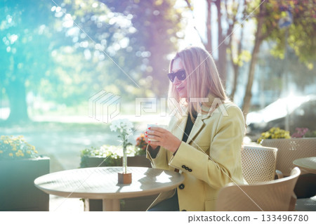 Woman enjoying coffee in a sunny outdoor cafe setting with flowers and trees 133496780